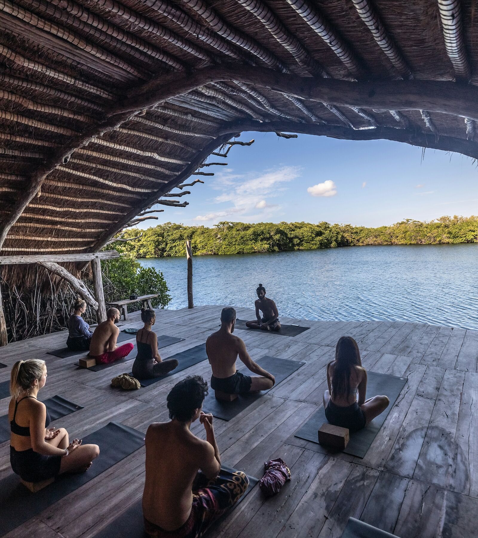 A guided yoga group gathered in an open-air retreat shala